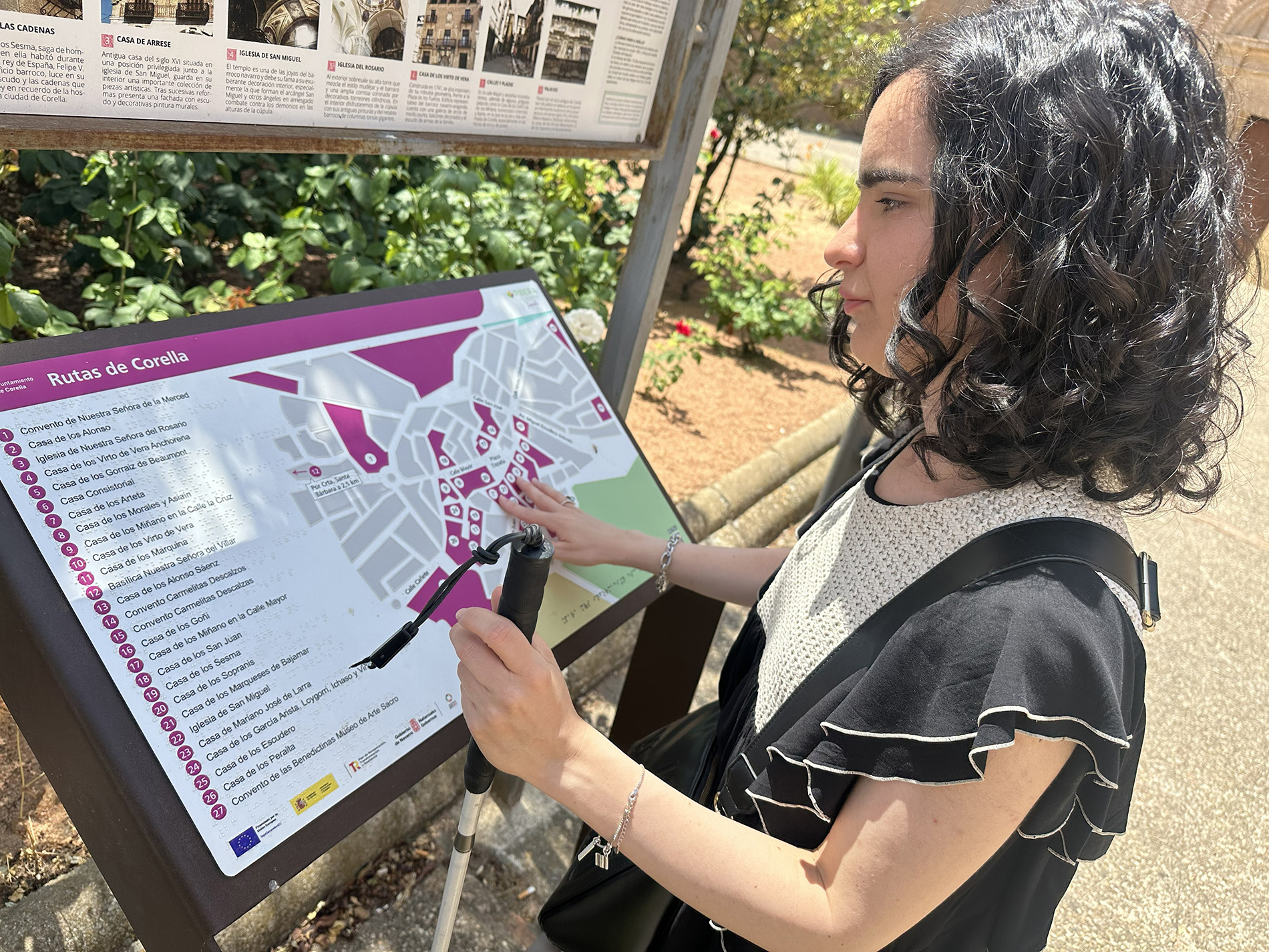 Mujer ciega usuaria de bastón blanco lee un plano háptico con las rutas turísticas de Corella. El plano incluye información en braille y vista.